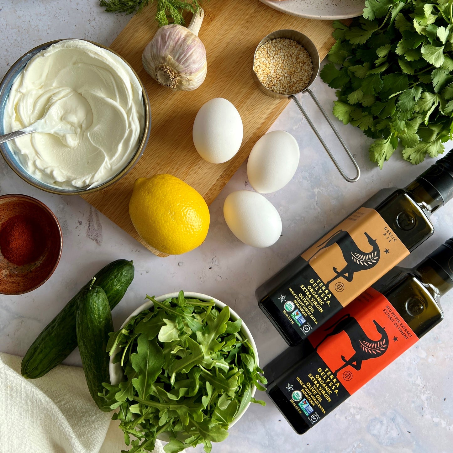 A scrumptious image of a traditional Turkish egg dish featuring perfectly poached eggs nestled atop a bed of creamy and garlicy yogurt, enhanced with a luscious Terra Delyssa Extra Virgin Olive Oil-infused chili, and sprinkled with fresh herbs.
