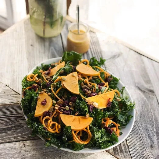 Salade de chou frisé massé avec nouilles de patates douces, kaki et vinaigrette à l'orange fumée