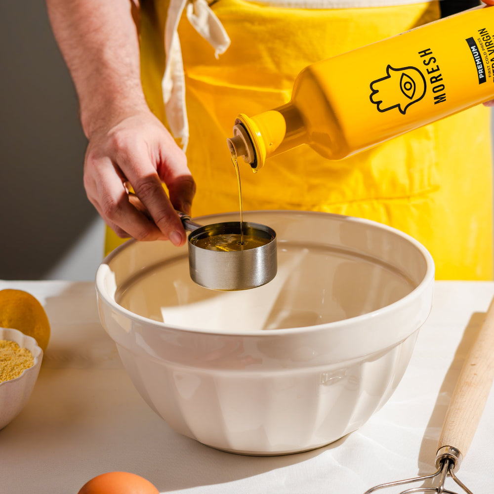 
                  
                    Person pouring Moresh olive oil from a bottle into a measuring cup over a bowl.
                  
                