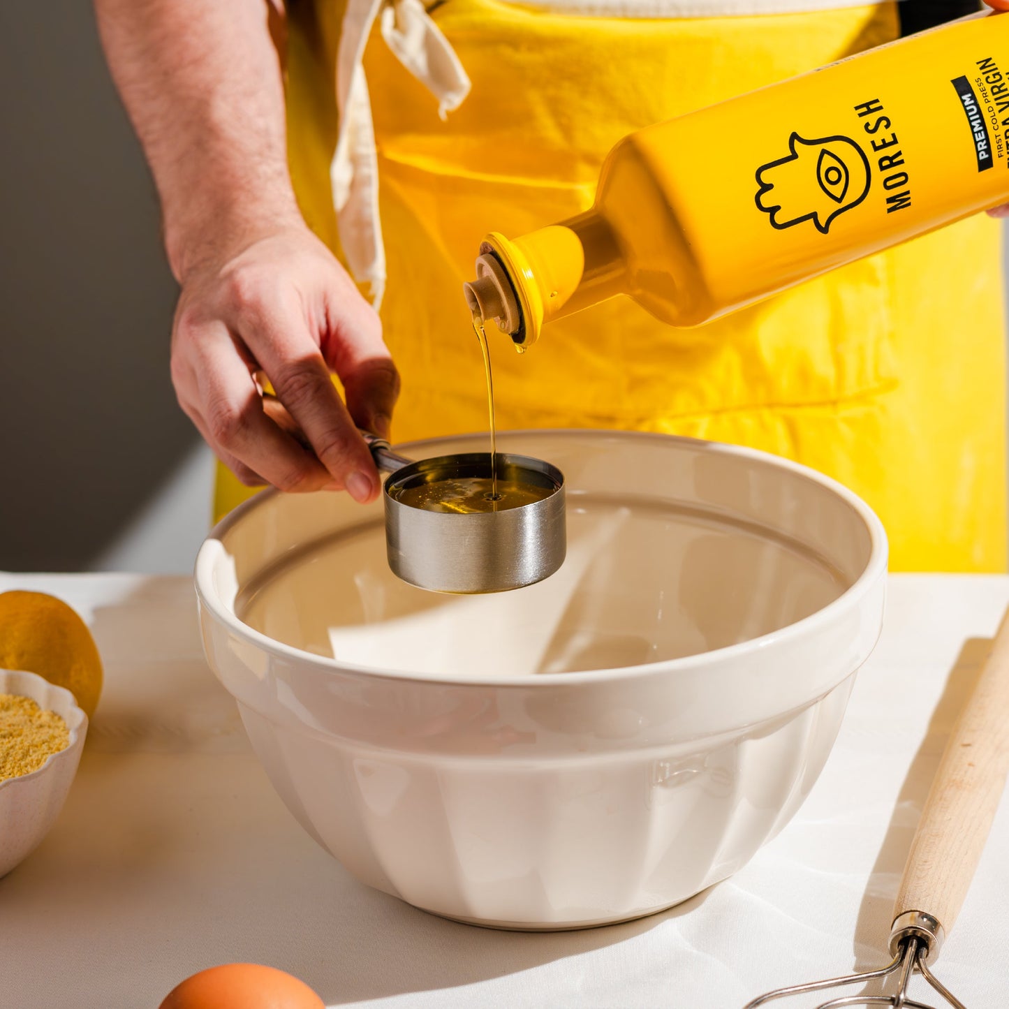 
                  
                    Person pouring Moresh olive oil from a bottle into a measuring cup over a bowl.
                  
                