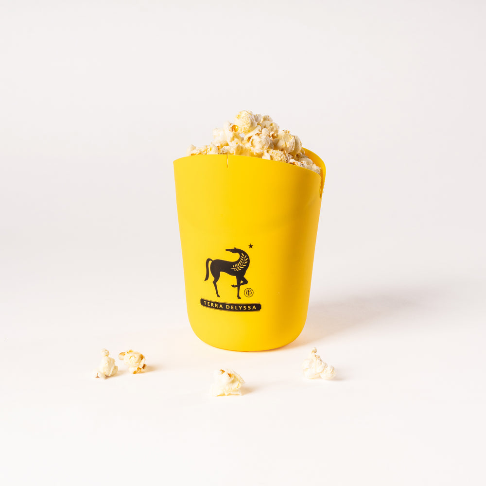 Front view of the yellow Terra Delyssa silicone popcorn popper with popcorn spilling out, featuring the brand’s horse logo prominently displayed.