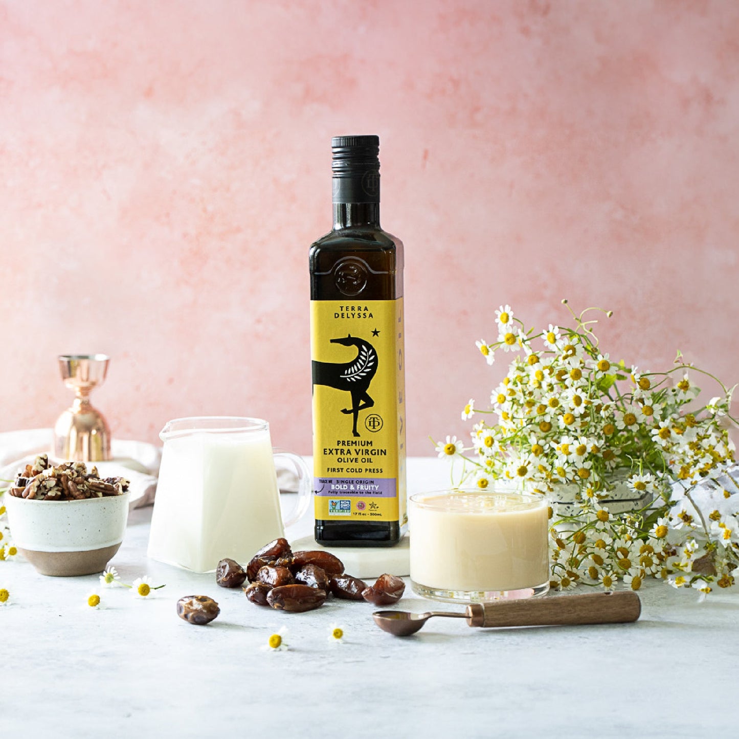 
                  
                    Bottle of best olive oil with a glass of milk, dates, and flowers on a light surface with a pink background
                  
                