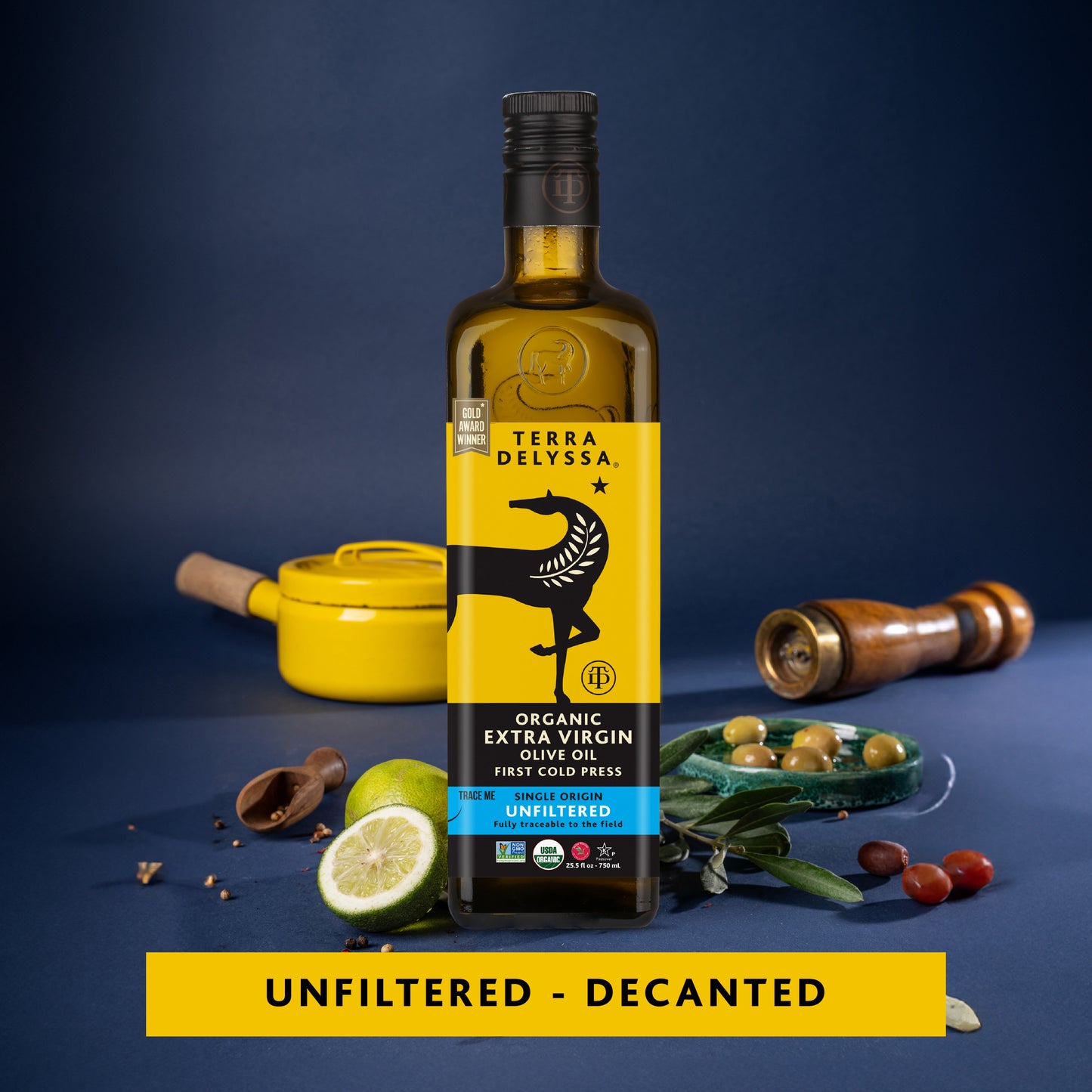 
                  
                    Bottle of Terra Delyssa organic extra virgin olive oil on a blue background with kitchen items.
                  
                
